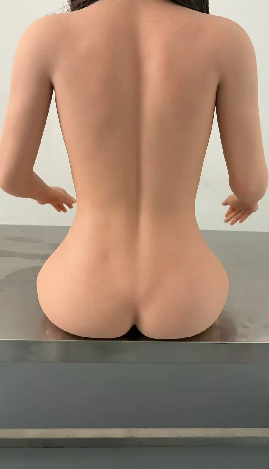 Factory reference rear close-up of Marisol doll seated on a metal workbench, showing her back, waist and hip contours.