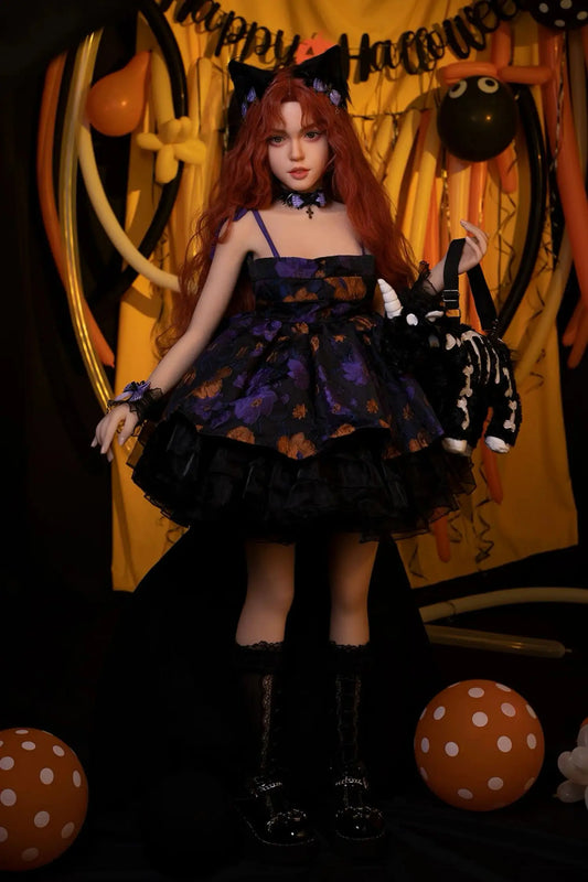 Amora sex doll full-body standing shot in Halloween party setting, long deep auburn red wavy curly hair, soft brown eyes with innocent direct gaze and natural nude lips, black lace choker necklace, black cat ear headband with purple gem detail, navy blue and purple Halloween pumpkin-print tiered ruffle babydoll spaghetti-strap dress with layered black tulle underskirt, purple floral wrist corsage, skeleton cat plush backpack held in one hand, black lace-top knee-high socks with black chunky platform Mary Ja