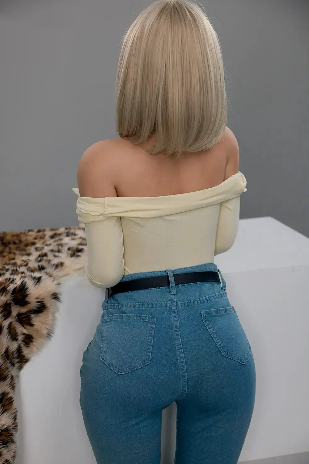 Rear view of Marisol blonde love doll in blue jeans and a black belt, with her cream top lowered below her shoulders.