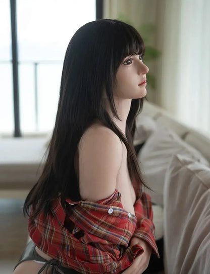 Rookie GND sex doll seated on sofa in red plaid shirt, black bangs, dark eyes, deep cleavage, realistic Asian companion doll by TopLoveDoll