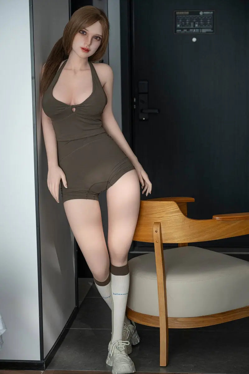 Gadora brunette companion doll standing beside a wooden chair in an olive romper, knee-high socks and sneakers