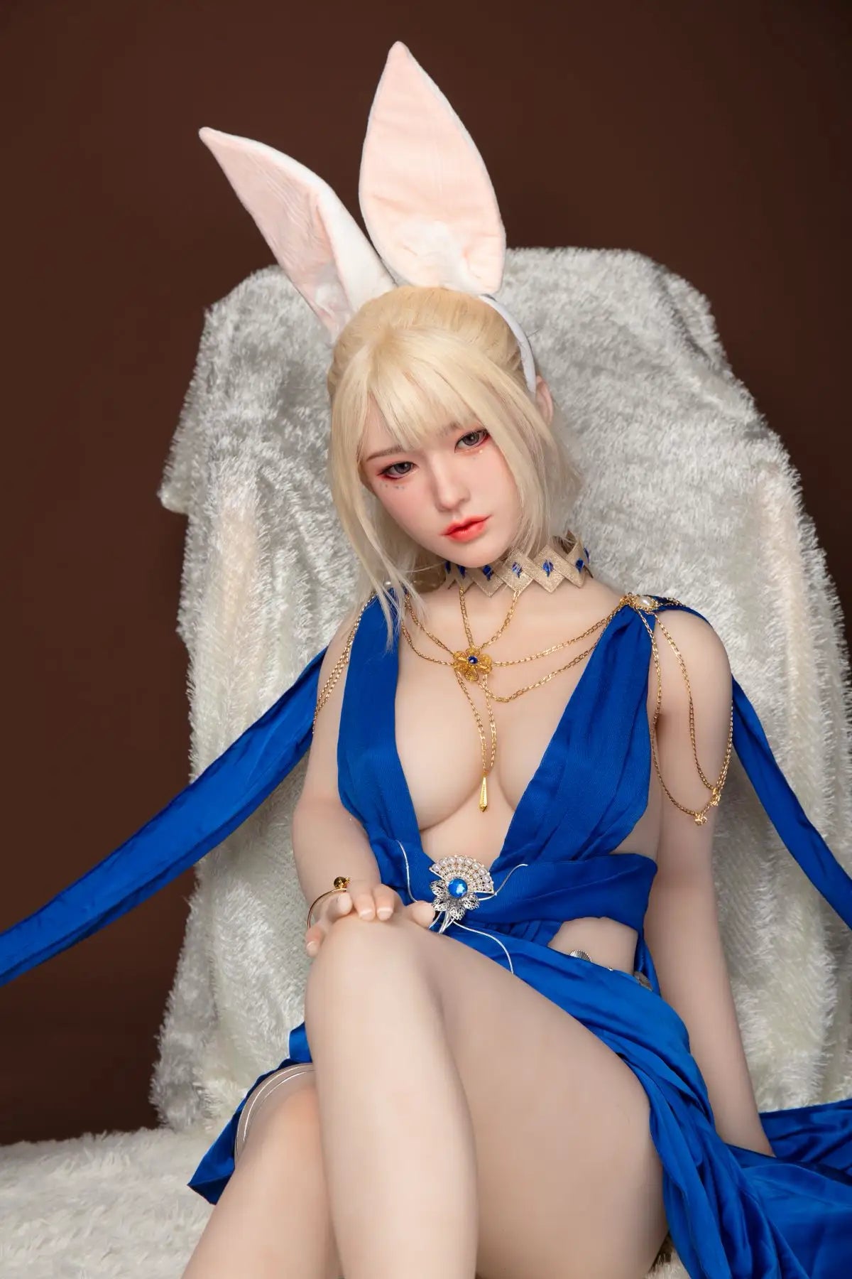 Olivia sex doll seated on white fluffy armchair black eyes long bright platinum blonde straight hair large white rabbit ear headpiece gold necklace bracelet royal blue deep-V cutout strap gown dress front slit gold heels dark brown studio background – full body seated shot – realistic slim asian GND white rabbit fantasy sex doll by TopLoveDoll
