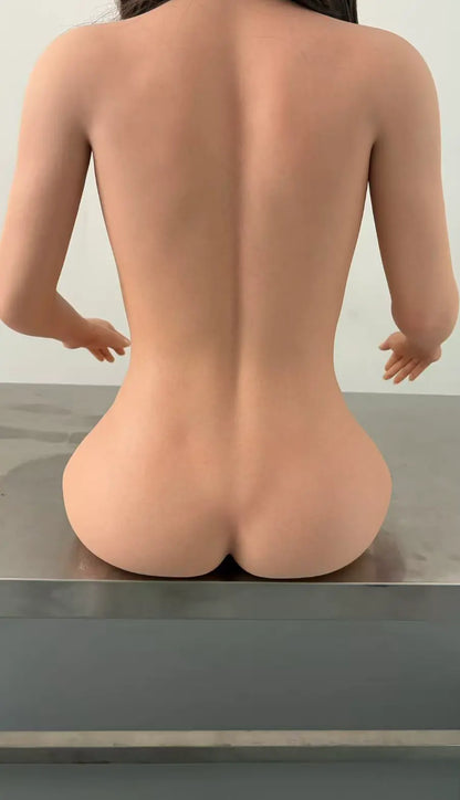 Factory reference rear close-up of Marisol doll seated on a metal workbench, showing her back, waist and hip contours.