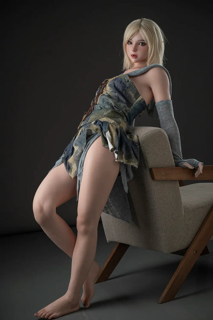 Full-length view of Elowen blonde elf doll leaning against an armchair in a lace-up fantasy dress with the hood lowered.
