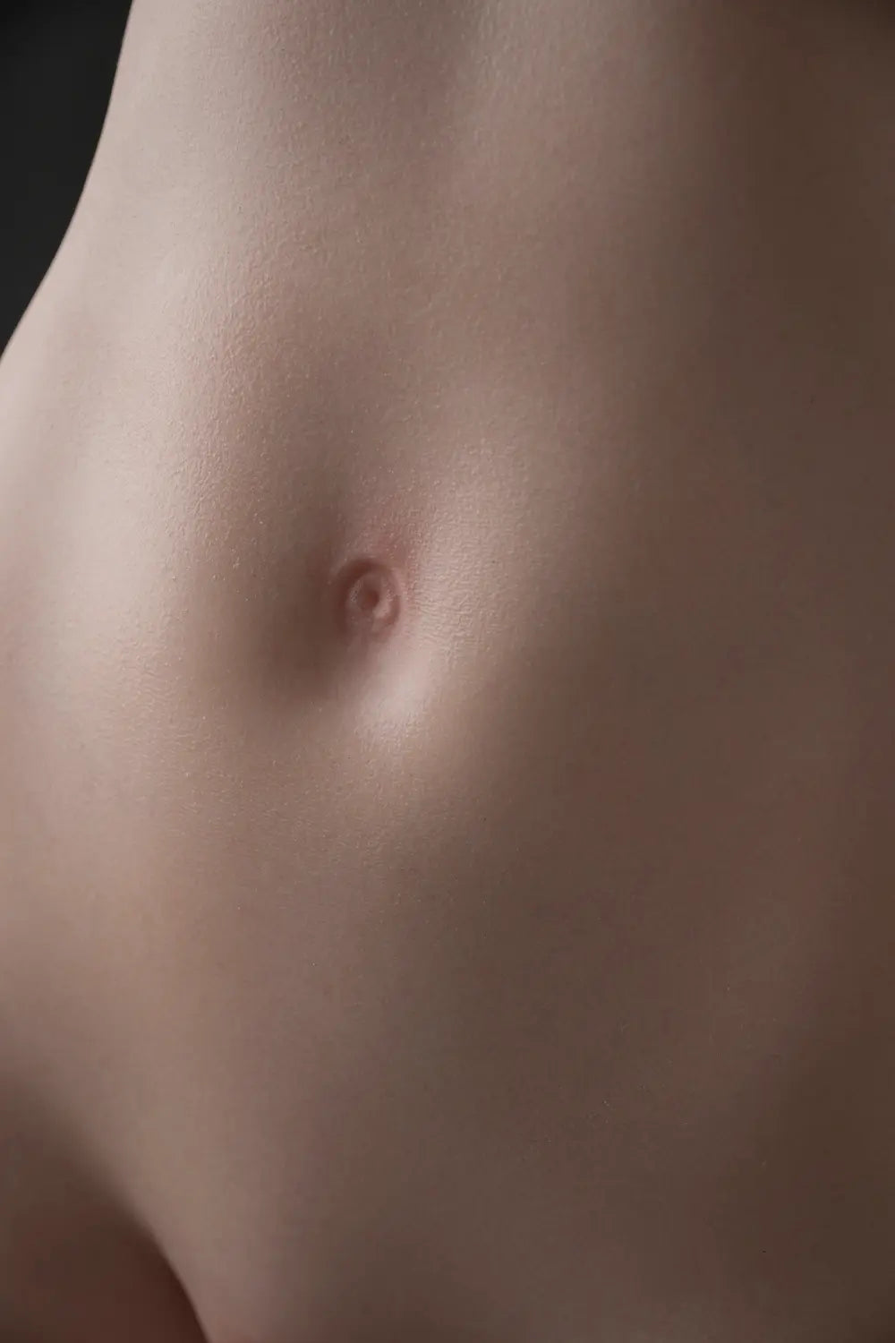 Close-up of Elowen doll's abdomen, showing the navel and surface texture under studio lighting.