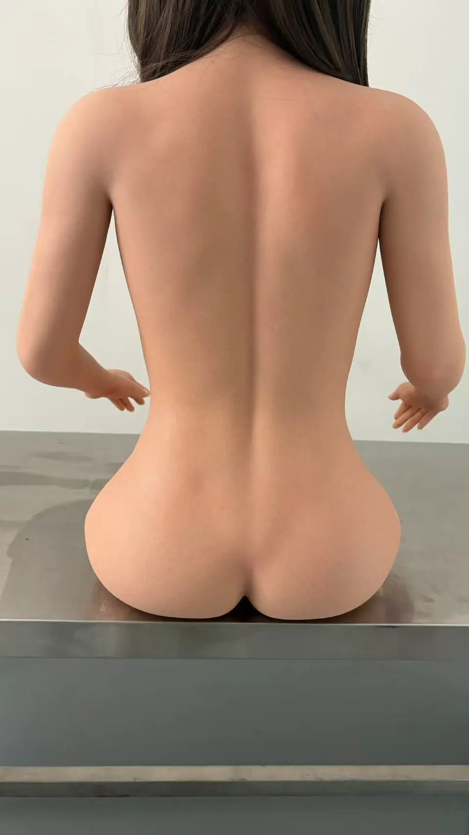 Factory reference rear view of Alina doll seated on a metal workbench, showing her back, waist and hip contours.
