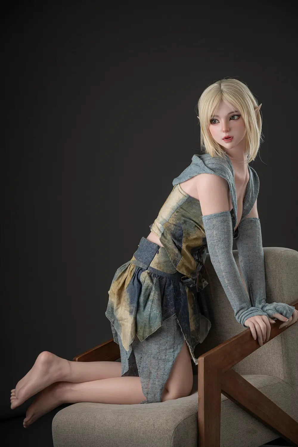 Side view of Elowen elf love doll kneeling on an armchair, holding the wooden armrest and looking to the side.