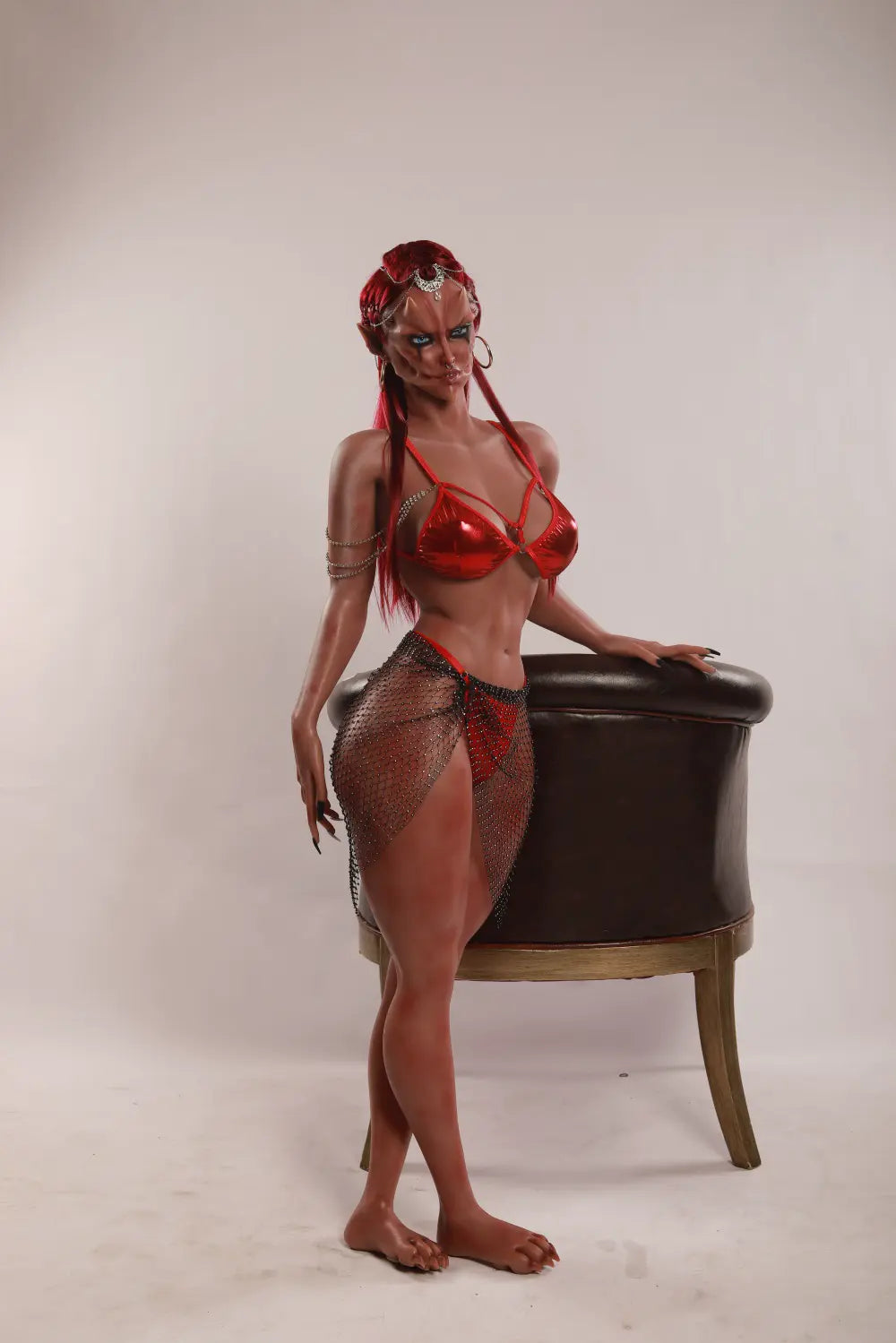 Full-length side view of Veyra sex doll standing beside a black-and-gold armchair in a red outfit