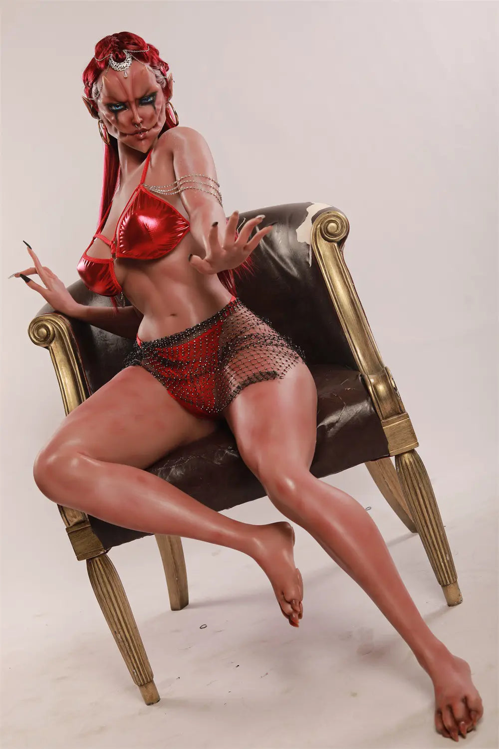 Wide three-quarter view of Veyra sex doll seated on an ornate armchair with one leg extended