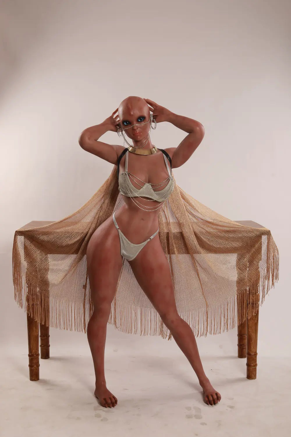 Vaelis alien sex doll standing with both hands beside the head in a silver outfit and gold-toned fringed cape