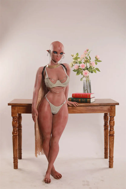Full-length view of Vaelis sex doll standing beside a wooden table with pink roses and stacked books