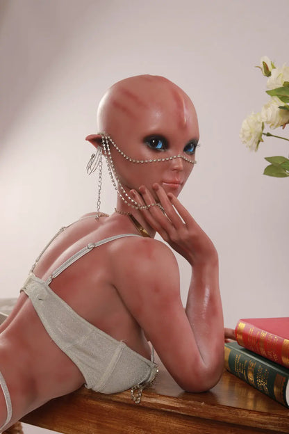 Over-the-shoulder portrait of Vaelis sex doll with face chains and books on a wooden table