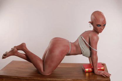 Side view of Vaelis sex doll kneeling on a wooden table with a silver top lowered and a red book nearby