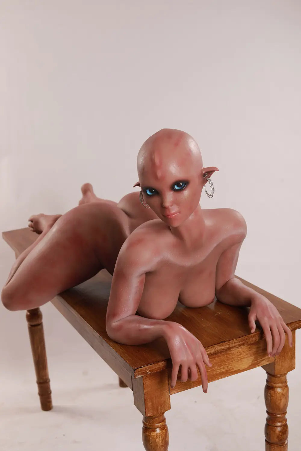 High-angle front view of Vaelis sex doll lying on a wooden table with bent legs