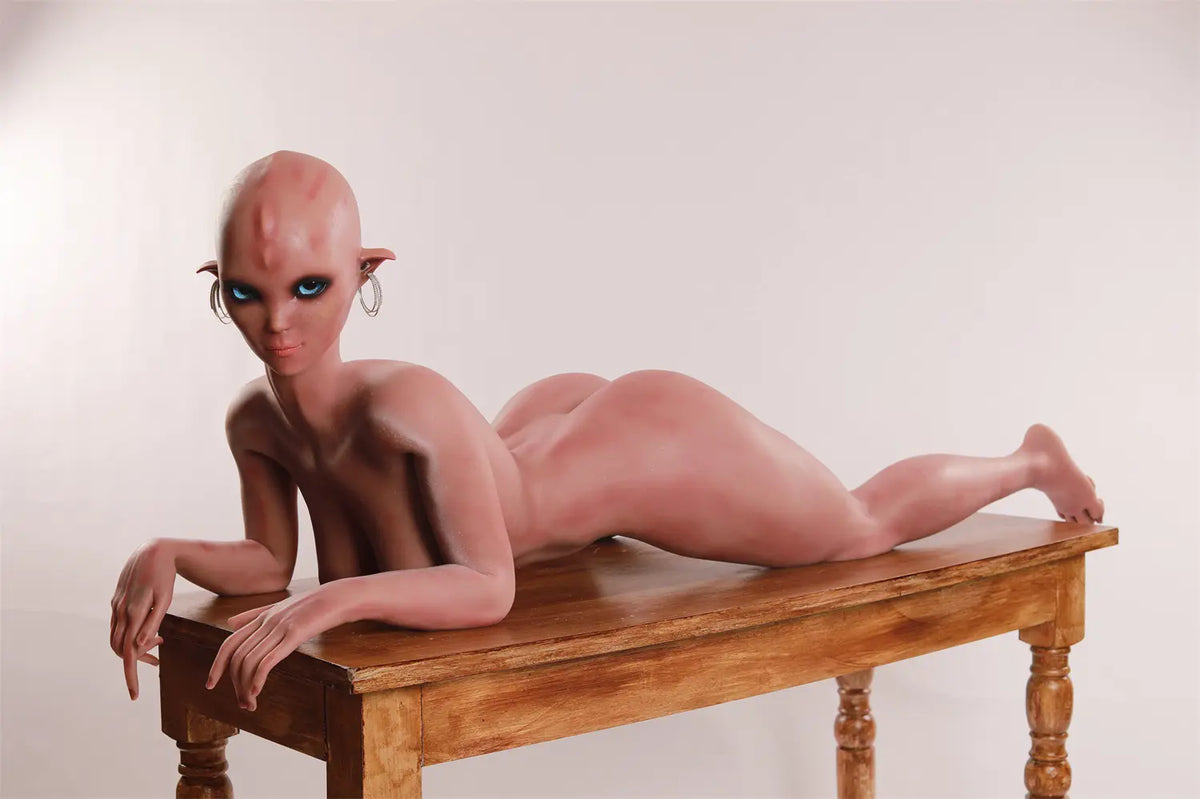 Wide side view of Vaelis sex doll lying on the stomach with forearms resting on a wooden table