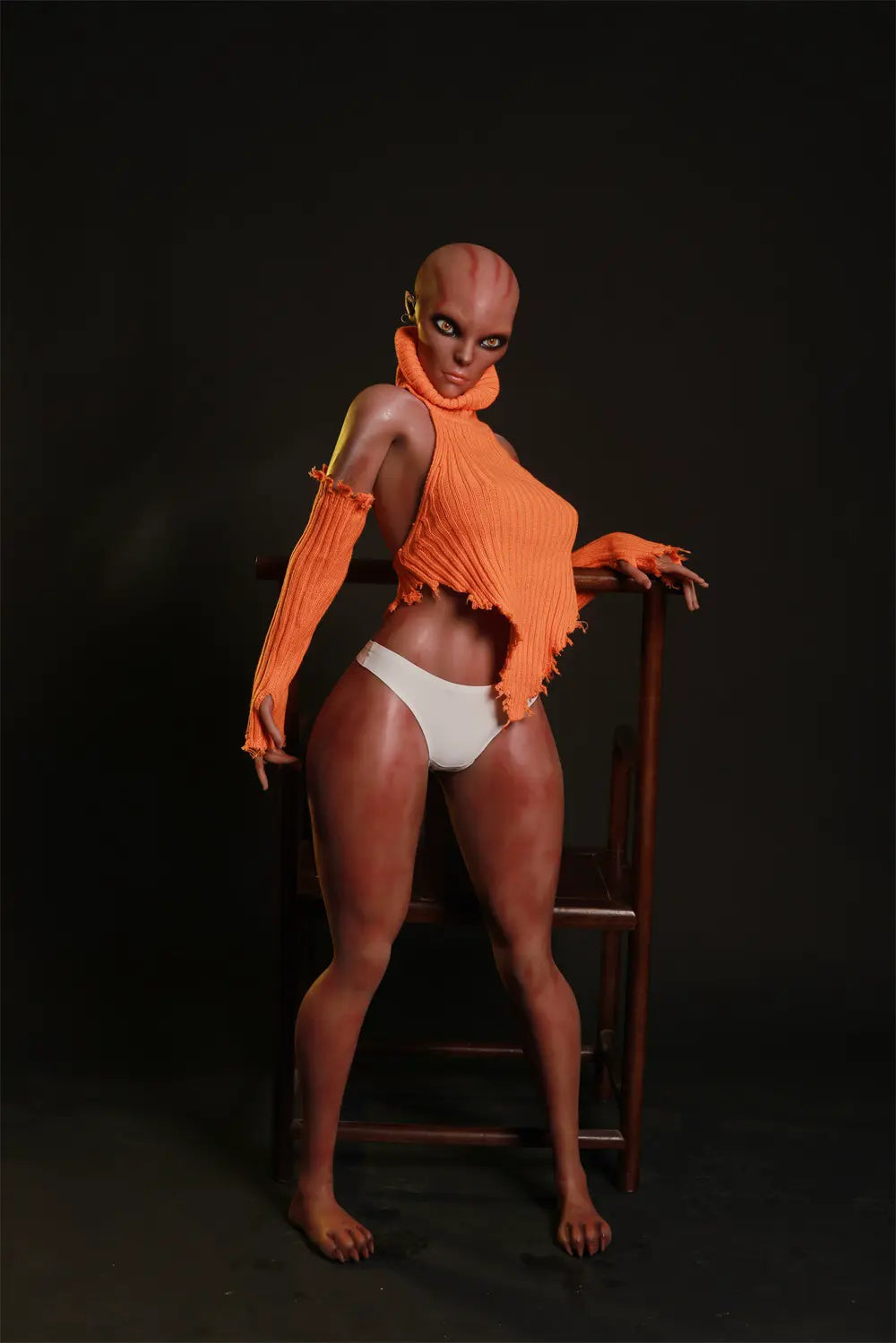 Nyxie alien sex doll standing beside a wooden chair in an orange knit top, matching sleeves and white briefs