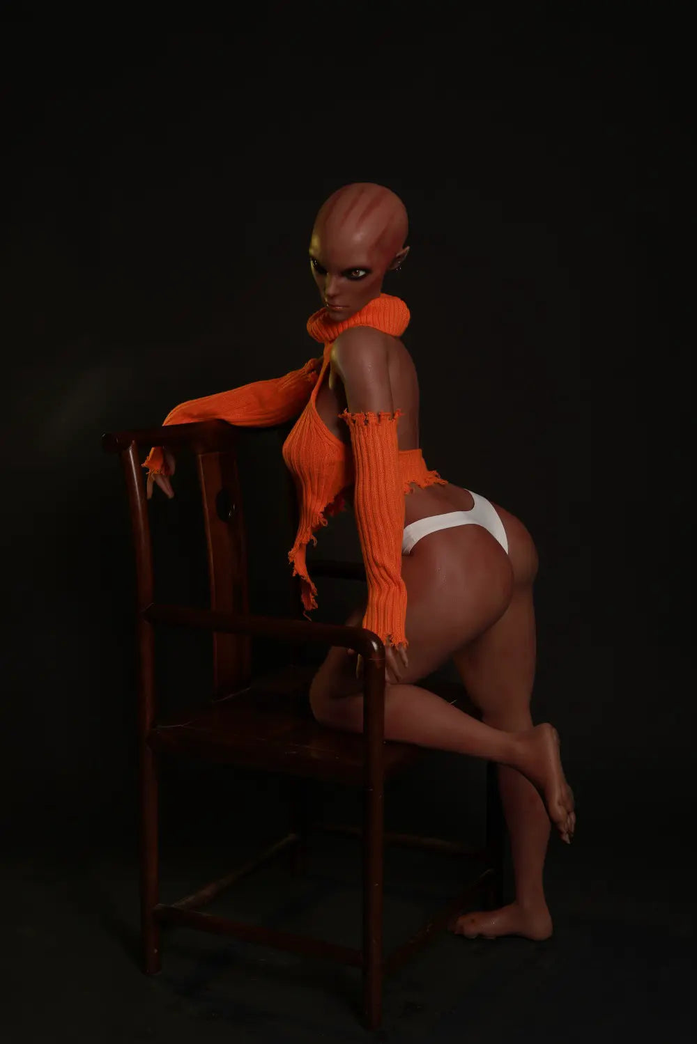 Nyxie alien sex doll looking over one shoulder with one knee resting on a wooden chair