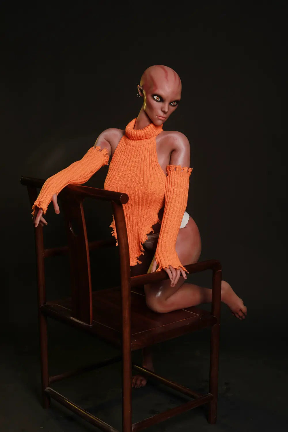 Nyxie alien sex doll kneeling on a wooden chair with hands resting on the wooden frame