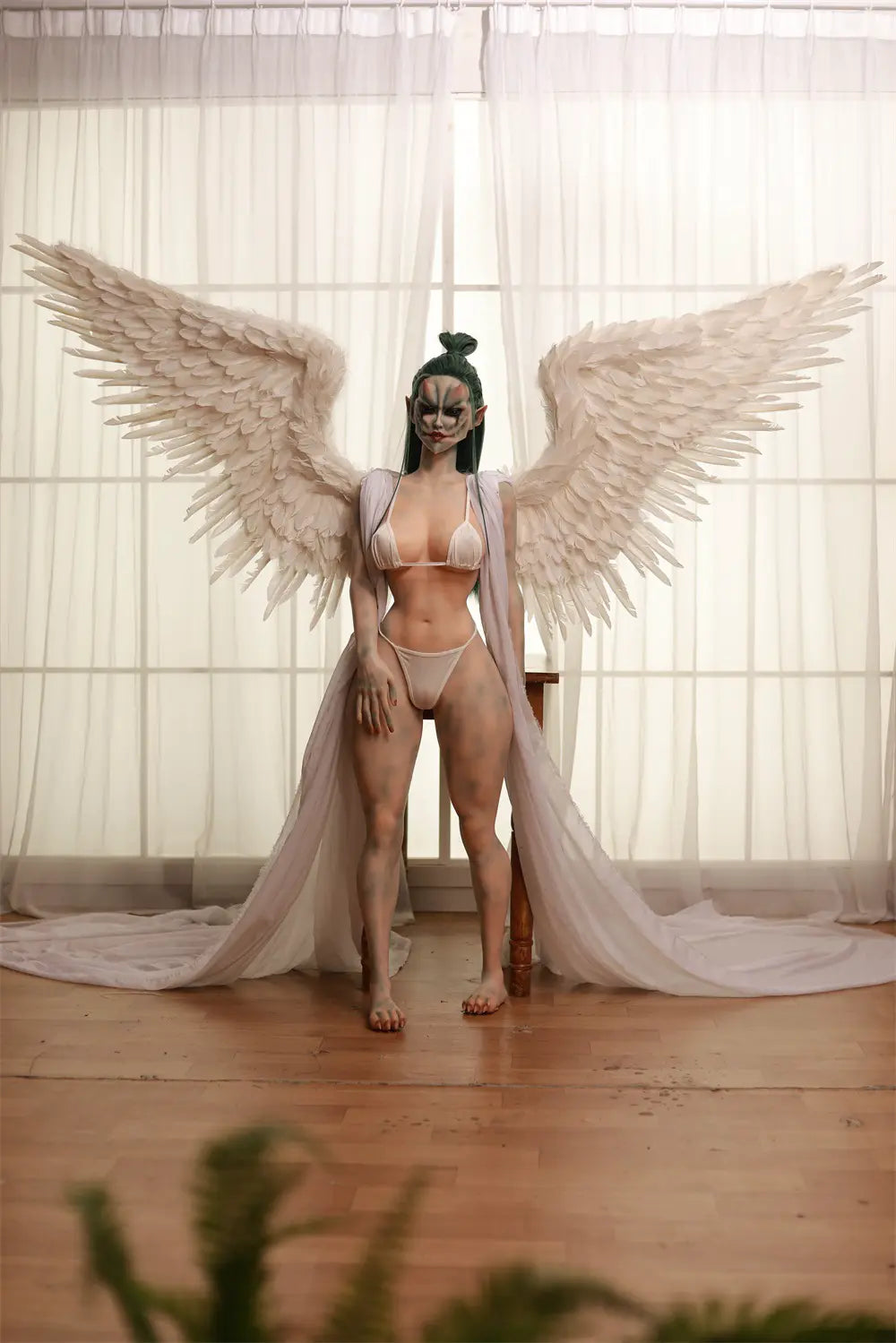 Full-length front view of Morveth dark wraith sex doll with white feathered wing accessories beside a bright window
