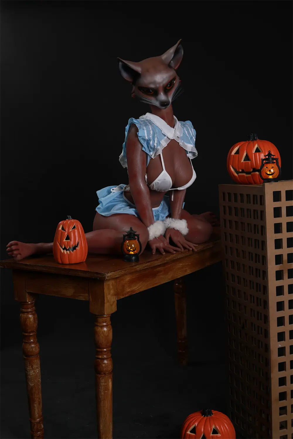 Vesper anthropomorphic fox sex doll seated among pumpkin decorations against a dark studio backdrop