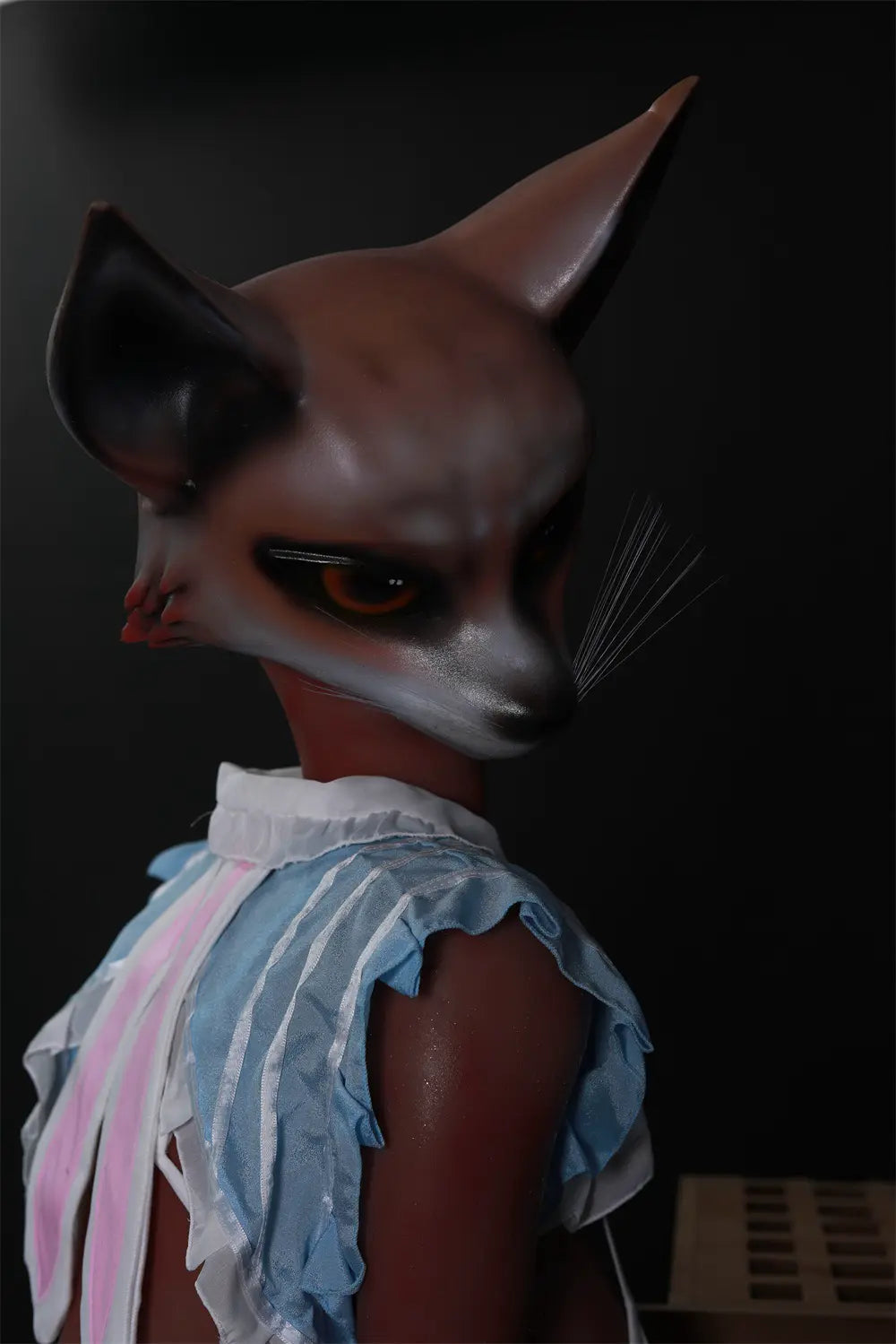 Close-up of Vesper fox sex doll looking over one shoulder, showing pointed ears, whiskers and blue costume ruffles
