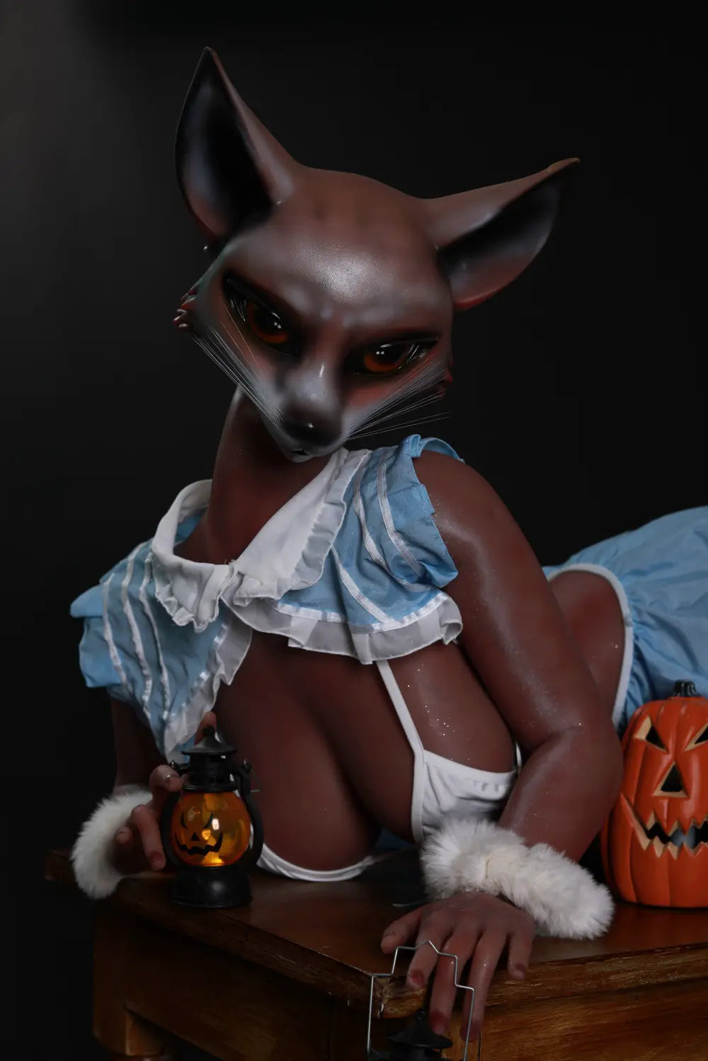 Closer view of Vesper fox sex doll resting on a wooden table with one hand holding a pumpkin lantern
