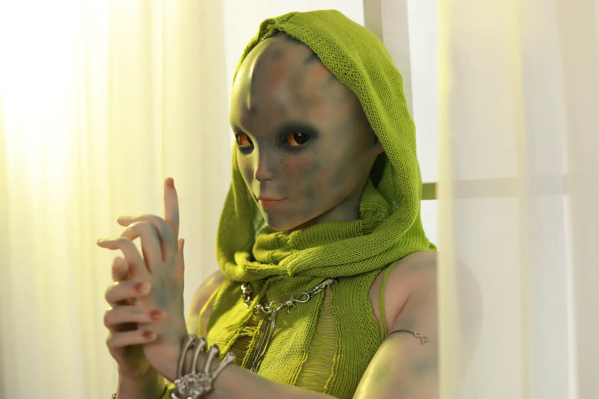 Front view of Sylvara sex doll in a green hood and leaf-like outfit with hands held near the chest