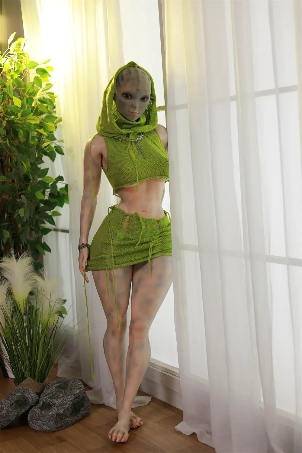 Portrait of Sylvara sex doll framed by a green hood with one hand raised beside the face