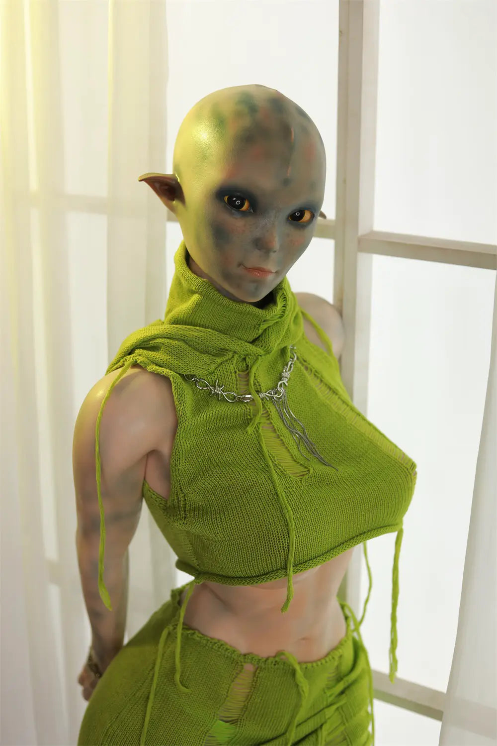 Rear three-quarter view of Sylvara sex doll showing the green hood and costume straps