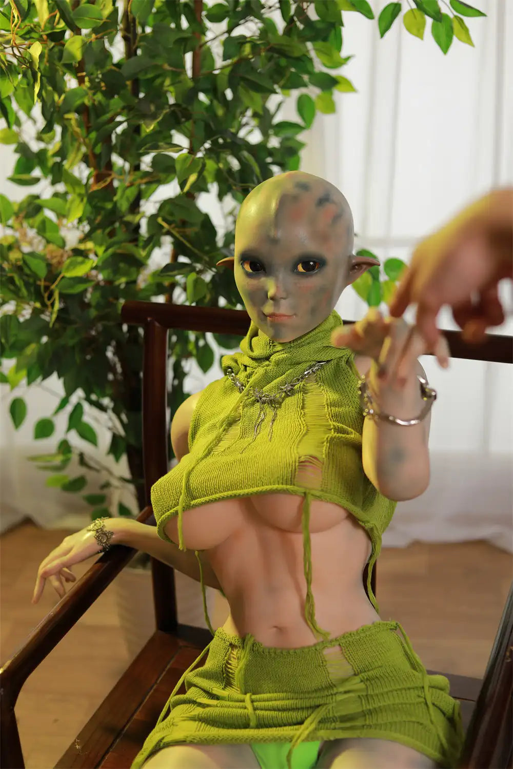 Closer portrait of Sylvara sex doll showing pointed ears, a hairless head and green costume details