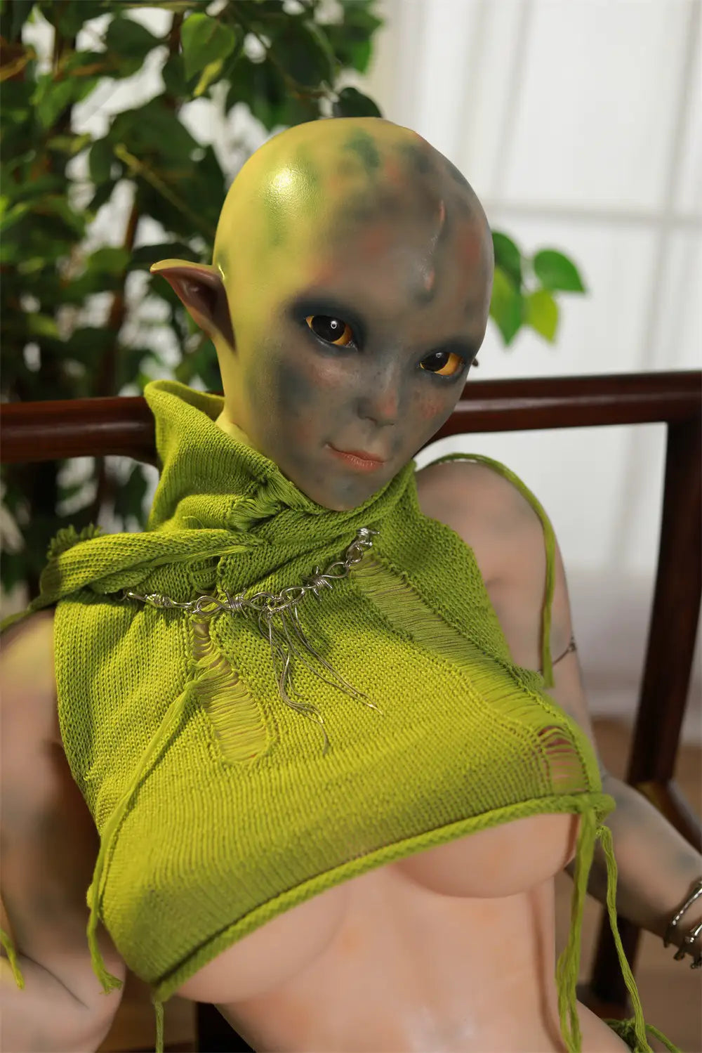 Closer seated view of Sylvara sex doll wearing a green leaf-like top