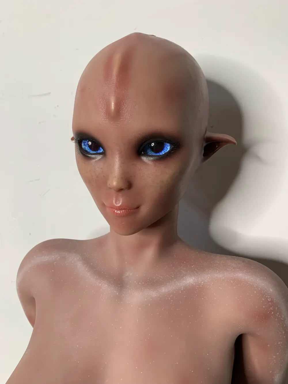 Factory close-up of Vaelis alien face showing blue eyes, dark eye surrounds and pointed ears