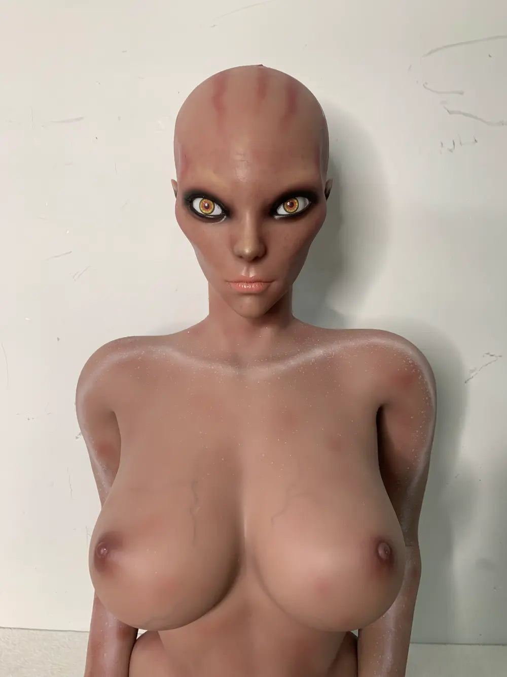 Front factory portrait of Nyxie sex doll showing the elongated head, dark eye surrounds and upper torso