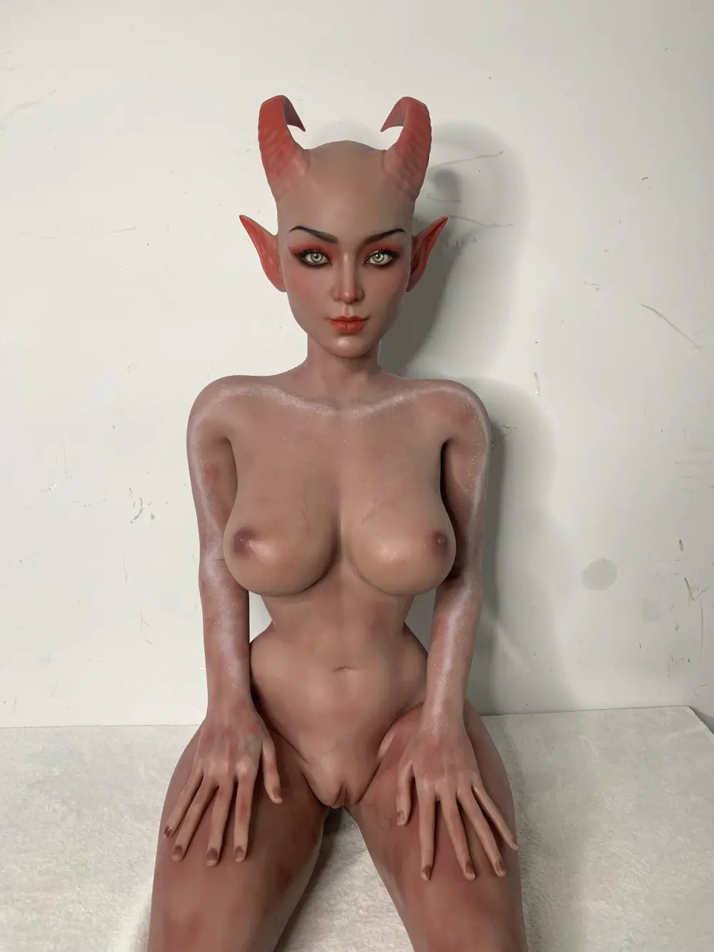 Factory reference photo of Tauris sex doll seated on a white-covered platform with hands on the thighs