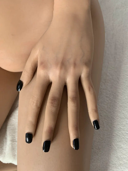 Factory detail photo of Vhaera sex doll's hand with dark fingernails resting on the thigh