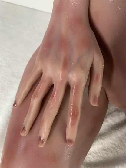 Factory close-up of Vesper sex doll's hand resting on the thigh, showing sculpted fingers and nails