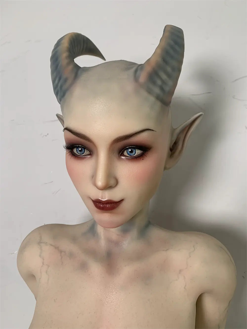 Factory close-up of Veltris sex doll's fantasy face showing the curved horns and dark eye surrounds